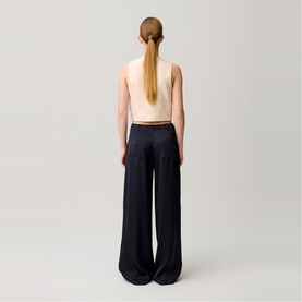 Model wearing navy wide-leg trousers, seen from behind, styled with a cream sleeveless top