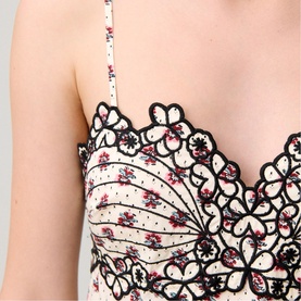 Close-up of a floral print cami top with black lace trim and scalloped neckline detail, small pink floral pattern on cream base