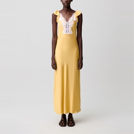 Model wearing yellow maxi slip dress with white lace-trimmed V-neckline and ruffle shoulders, styled with dark brown sandals