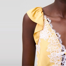 Model wearing yellow satin dress with white lace trim and ruffle shoulder detail, deep V-neckline visible