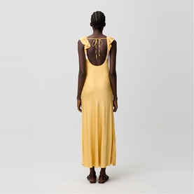 Model wearing yellow sleeveless maxi dress with ruffle shoulder straps and open back tie detail, back view