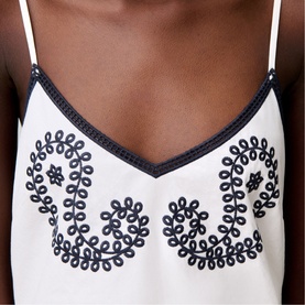 Model wearing white cami top with navy floral embroidery detailing and contrast trim neckline and straps