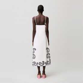 Model wearing white midi slip dress with black paisley embroidery at hem, styled with pink strappy sandals, back view