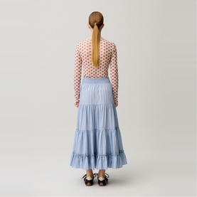 Model wearing a light blue tiered maxi skirt with a pink polka dot long-sleeve top and black mary jane shoes, seen from behind.