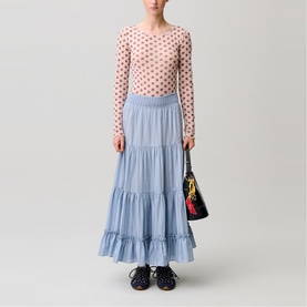 Model wearing light blue tiered maxi skirt with pink polka dot top, carrying small dark floral bag, with navy lace-up shoes