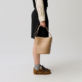 Model carrying Claude Pierlot bucket bag in clear tan leather, single top handle, styled with black skirt and striped blouse