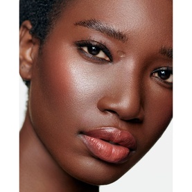 Model wearing Chanel Multi-Use Duo Stick in Pure Glow, shown as a warm bronzed flush on cheeks and glossy nude-brown lip colour.