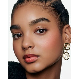 Model with Chanel Multi-Use Duo Stick in Pure Glow blush, worn as a warm rosy flush on cheeks, styled with gold Chanel No.5 drop earrings