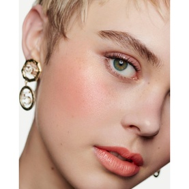 Model with Chanel Multi-Use Duo Stick in Pure Glow, showing soft coral blush on cheeks and matching lip colour, with gold drop earrings