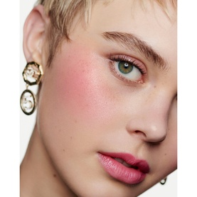 Model with Chanel Multi-Use Duo Stick in Pure Glow, showing blush applied to cheeks and lips; gold circular drop earrings visible