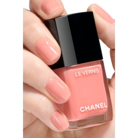 Chanel Le Vernis Longwear Nail Colour in Party Girl, a soft coral-pink varnish, shown held between fingers with matching manicure