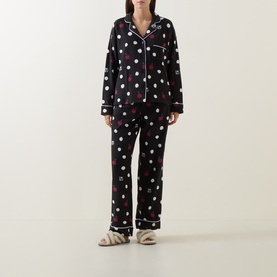 Model wearing DKNY Dotted Apple Pyjamas in black with apple and spot print, contrast piping, notched collar, styled with cream slider sandals.