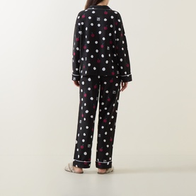 Model wearing DKNY Dotted Apple Pyjamas in black with white and red apple and polka dot print, contrast piping trim, long sleeves, back view