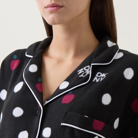 Model wearing DKNY Dotted Apple Pyjamas in black, showing notched collar, white contrast piping, and multicoloured apple and dot print.