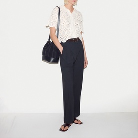 Model wearing Jigsaw navy wide-leg trousers with white broderie anglaise top, tan belt, and black sandals, carrying a black bucket bag.