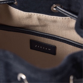 Jigsaw navy bag interior view showing beige herringbone lining and silver-tone hardware detail with brand logo patch.