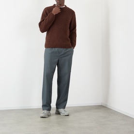 Model wearing Edwin Crew Neck knit in Rum Raisin, styled with grey wide-leg trousers and light grey trainers.