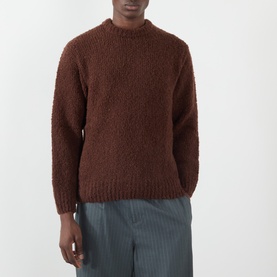 Model wearing Edwin Crew Neck jumper in Rum Raisin, chunky boucle knit, styled with grey stripe trousers.
