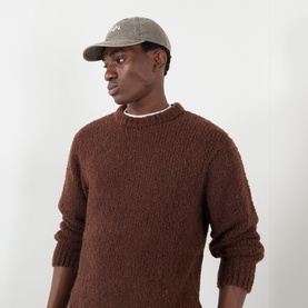 Model wearing Edwin Crew Neck knit jumper in Rum Raisin brown, styled with a grey cap and white crew neck tee.