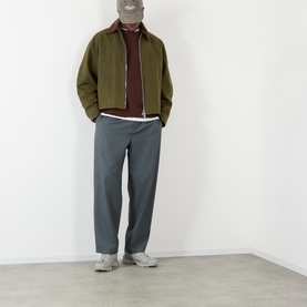 Model wearing Edwin Rum Raisin crew neck knit, styled with olive zip jacket, grey trousers and grey trainers.
