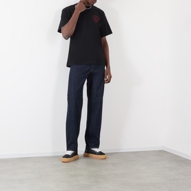 Model wearing Edwin Crew Neck T in black with dark indigo jeans and canvas trainers with gum soles.