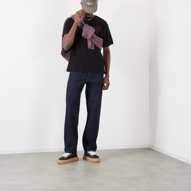 Model wearing Edwin black crew neck T-shirt with dark indigo jeans and tan-soled trainers, holding a mauve bag.