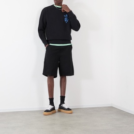 Model wearing Edwin black cotton sweatshirt with blue graphic, styled with matching black shorts and canvas trainers with gum soles.