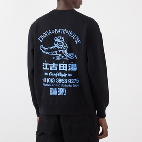 Model wearing Edwin black cotton sweatshirt, back view, with blue Japanese graphic and Ekoda Bath House print. Styled with black trousers.