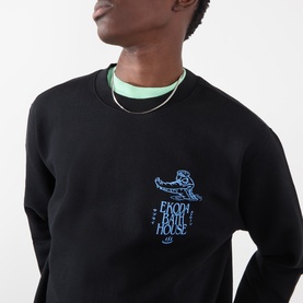 Model wearing Edwin black cotton sweatshirt with blue Barriohouse graphic print on chest, styled with mint green underlayer and silver chain necklace.