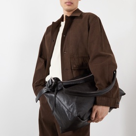 Model carrying Lemaire dark chocolate veal leather bag with oversized knotted handle, styled with brown jacket and trousers