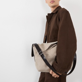 Model carrying Lemaire Belted Tote Bag in dark linen canvas with black adjustable leather shoulder strap and silver-tone hardware, styled with brown