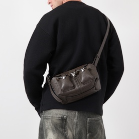 Model carrying Lemaire Mini Soft Gear Shoulder Bag in dark green leather, silver-toned clasps, worn as crossbody, styled with black sweatshirt