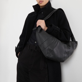 Model carrying Lemaire Croissant Large Bag in black leather with silver-tone hardware, styled with black coat and trousers