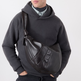 Model carrying Lemaire Large Croissant Shoulder Bag in dark chocolate leather, worn crossbody, with grey hoodie styled alongside.
