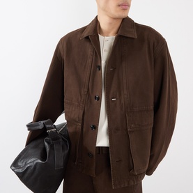 Model wearing Lemaire Flap Pocket Overshirt in brown cotton with point collar and flap pockets, styled with matching trousers, carrying black bag.
