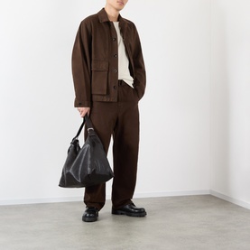Model wearing Lemaire Flap Pocket Overshirt in brown cotton with matching trousers, styled with a black tote bag and black loafers.