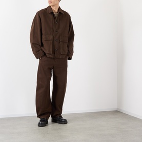 Model wearing Lemaire Belted Casual Trousers in brown, styled with matching brown cotton jacket and black leather shoes.
