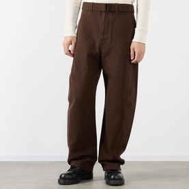 Model wearing Lemaire Belted Casual Trousers in brown, straight-leg fit with matching belt, styled with a cream top and black loafers.