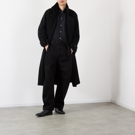 Model wearing Lemaire black cotton casual trousers, styled with a long black overcoat, black shirt and black leather shoes.