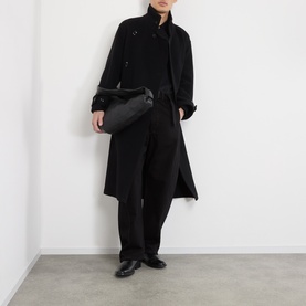 Model wearing Lemaire black cotton casual trousers, styled with a black coat, crossbody bag, and black leather shoes.