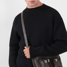 Model wearing Lemaire black wool crew neck jumper with ribbed cuffs and collar, styled with a dark crossbody bag.