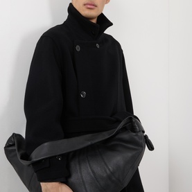 Model wearing Lemaire black wool coat with double-breasted button front and funnel neck, styled with a black leather bag.