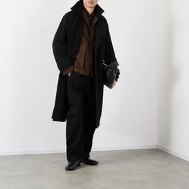 Model wearing Lemaire black wool coat, styled with brown knit, black trousers and leather shoes, carrying small black bag.
