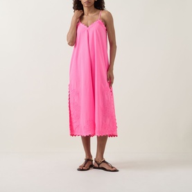 Model wearing Juliet Dunn hot pink cotton midi dress with scalloped hem, thin straps and side cutwork detail, styled with brown sandals
