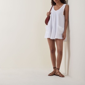 Model wearing Embroidered Low Back Mini Dress in white with scalloped hem, styled with brown strappy sandals and a brown shoulder bag.