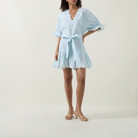 Model wearing Juliet Dunn Poplin Tie Waist Dress in Ice Blue/White, mini length with ruffled hem, sleeves and self-tie waist, styled with tan sandals