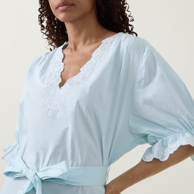 Model wearing Poplin Tie Waist Dress in Ice Blue with white lace trim at V-neckline and ruffled short sleeves, close-up detail shot.