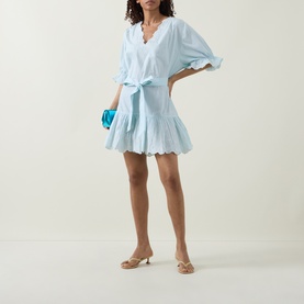 Model wearing Juliet Dunn Poplin Tie Waist Dress in Ice Blue/White with ruffled hem and sleeves, styled with nude heels and blue clutch bag.