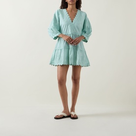 Model wearing Juliet Dunn Tiered Scalloped Dress in pistachio with V-neckline and scalloped trim, styled with tan flat sandals