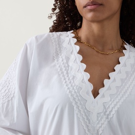 Model wearing Juliet Dunn white cotton dress with scalloped lace V-neckline trim, styled with a gold chain-link necklace.